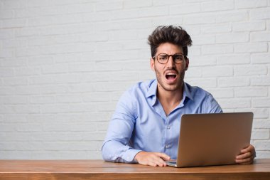 Oturma ve çalışma üstünde a laptop çok kızgın ve üzgün, çok gergin, öfkeli, negatif ve çılgın çığlık genç iş adamı