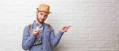 Genç yolcusu adam giyen sırt çantası ve tarafına işaret eden bir vintage fotoğraf makinesi, gülümseyen bir şey, doğal ve rahat sunan şaşırttı. Bir uçak model holding.