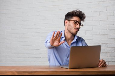 Oturan genç iş adamı ve çalışma üstünde a laptop ciddi ve kararlı, önde, el koyarak durdurmak jest, kavramı inkar