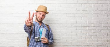 Sırt çantası ve bir vintage kamera gösteren iki numaralı sayma simgesi, matematik, kendinden emin ve neşeli kavramı giyen genç yolcusu adam. Biletin holding.