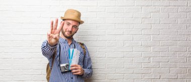 Sırt çantası ve bir vintage kamera gösteren üç numaralı sayma simgesi, matematik, kendinden emin ve neşeli kavramı giyen genç yolcusu adam. Biletin holding.