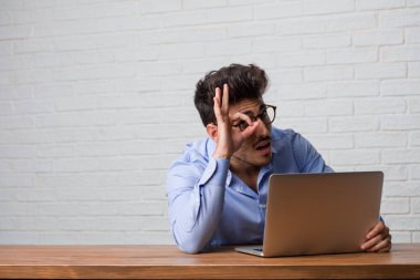 Oturma ve çalışma üstünde a laptop neşeli ve heyecanlı ve çığlık, onay ve başarı kavramı ok jest yapıyor kendine güvenen genç iş adamı