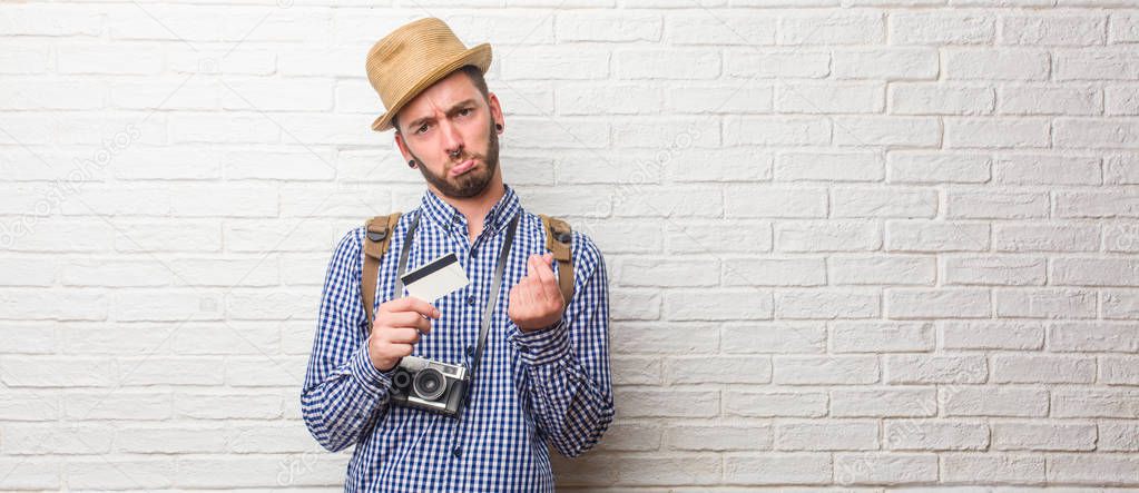 Young traveler man wearing backpack and a vintage camera sad and depressed, making a gesture of need, restoring to charity, concept of poverty and misery. Holding a credit card.