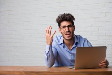 Oturma ve çalışma üstünde a laptop çok korkmuş ve korkmuş, çaresiz için bir şey acı çığlıkları ve açık gözler, Genç iş adamı delilik kavramını