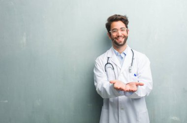 Gülümseyen ve neşeli, bir ürün gösteren genç dostu Doktor adam el ile bir şey tutan bir kopya alanı ile bir grunge duvara hayali bir nesne sunan