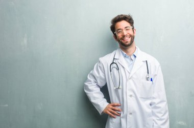 Genç dostu Doktor adam ile el HIPS, ayakta, rahat ve gülümseyen, çok olumlu ve neşeli bir kopya alanı ile bir grunge duvara