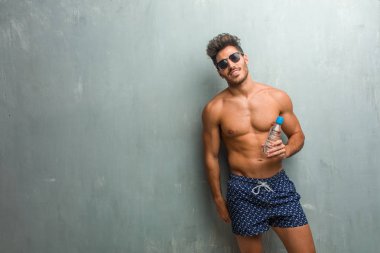 Pozitifliği ve başarı bir grunge duvara neşeli ve büyük bir gülümseme ile kendinden emin, samimi ve içten, bir mayo giyen genç atletik adam ifade