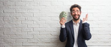 Rahat ve neşeli, gülen ve having fun, beyaz tuğla duvara bir takım elbise giymiş genç iş adamı kendinden emin ve başarılı hissediyor