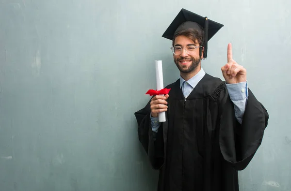 Young graduated man against a grunge wall with a copy space showing number one, symbol of counting, concept of mathematics, confident and cheerful