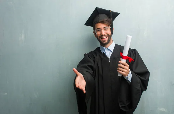 Young graduated man against a grunge wall with a copy space reaching out to greet someone or gesturing to help, happy and excited