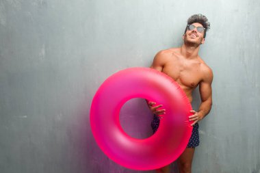 Rahat ve neşeli, gülen ve having fun, grunge duvara bir mayo giyen genç atletik adam kendinden emin ve başarılı hissediyor