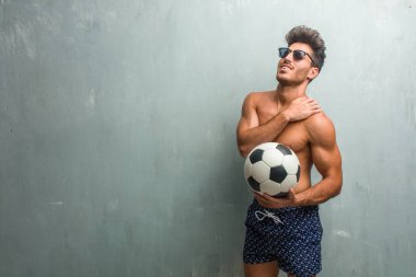 Young athletic man wearing a swimsuit against a grunge wall with back pain due to work stress, tired and astute clipart