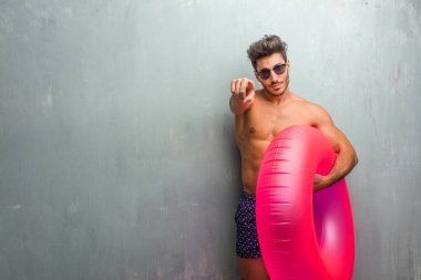 Bir grunge duvara neşeli ve gülümseyerek önüne işaret eden bir mayo giyen genç atletik erkek