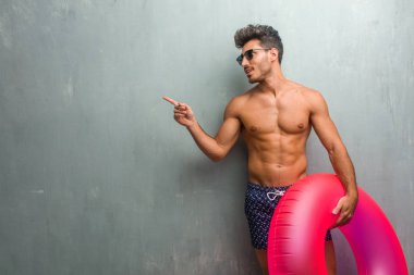 Sürpriz bir şey, doğal ve rahat sunan gülümseyen tarafına işaret eden bir grunge duvara bir mayo giyen genç atletik adam
