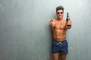 Neşeli ve heyecanlı, grunge duvara bir mayo giyen genç atletik erkek gülümseyen parmağını yukarı, başarı ve onay, kavram yükselterek ok ve jest