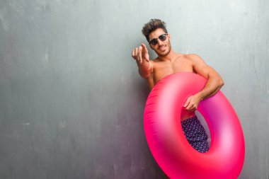 Bir grunge duvara neşeli ve gülümseyerek önüne işaret eden bir mayo giyen genç atletik erkek