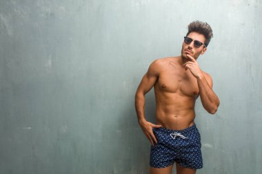 Bir grunge duvar şüphe ve karışık, düşünme, bir fikir ya da bir şey hakkında endişeli karşı bir mayo giyen genç atletik erkek