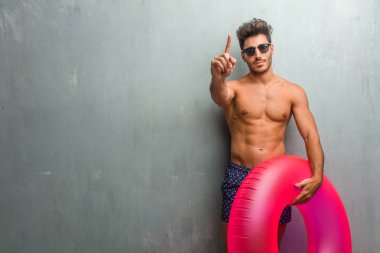 Gösterilen bir numaralı simgesi sayma, kavramı matematik, kendinden emin ve neşeli bir grunge duvara bir mayo giyen genç atletik adam