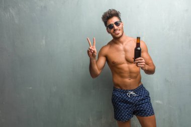 Bir grunge karşı bir mayo giyen genç atletik erkek duvar eğlenceli ve mutlu, pozitif ve doğal, zafer, barış kavramı bir jesti yapıyor