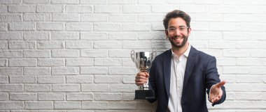 Birisi ya da el hareketi, mutlu ve heyecanlı yardımcı olmak için selamlıyorum uzanarak bir beyaz tuğla duvara bir takım elbise giymiş genç iş adamı