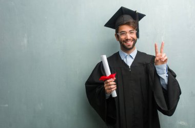 Genç adam bir grunge duvara gösterilen iki numaralı sayma simgesi, matematik, kendinden emin ve neşeli kavramı kopya alanı ile mezun.