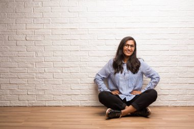 Genç Hintli kadın kalça, rahat ve gülümseyen, çok olumlu ve neşeli ayakta, el ile bir tuğla duvara oturup