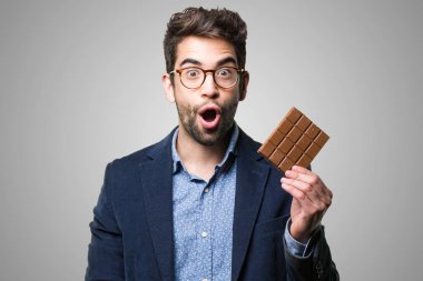 Çikolata gri arka plan üzerinde tutarak şaşırmış genç adam