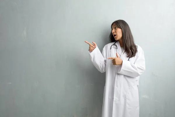 Young indian doctor woman against wall pointing to side