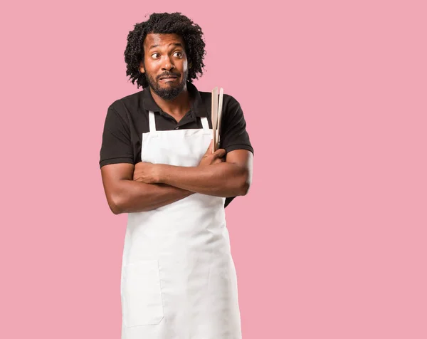 Handsome african american baker doubting and shrugging shoulders, concept of indecision and insecurity, uncertain about something