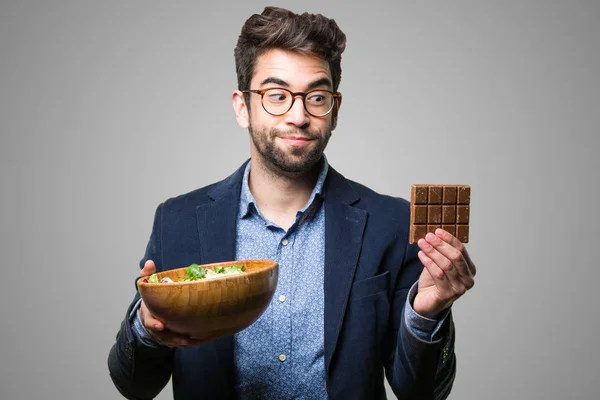 Mladý Muž Volba Mezi Čokolády Salát Šedém Pozadí — Stock fotografie