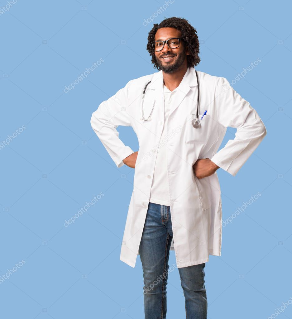 Handsome african american medical doctor with hands on hips, standing, relaxed and smiling, very positive and cheerful