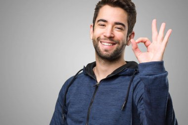 Genç adam gri arka plan üzerinde iyi jest yapıyor