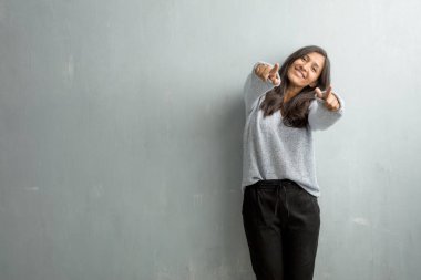 Grunge duvara neşeli ve gülümseyerek açık için işaret eden genç Hintli kadın