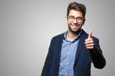 Genç adam gri arka plan üzerinde başparmak ile ayakta