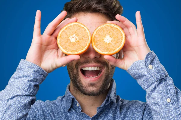 Молодой Человек Закрывает Глаза Апельсинами Синем Фоне — стоковое фото