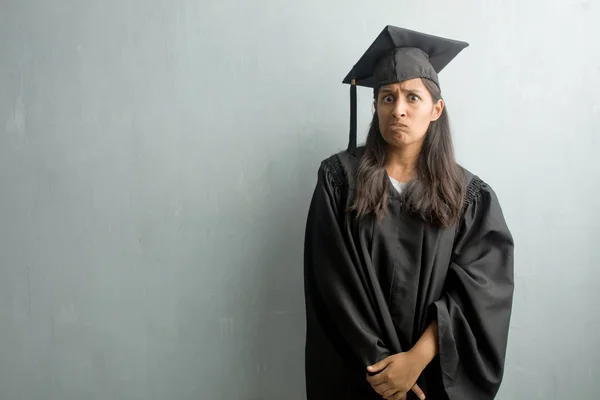 Young graduated indian woman against a wall worried and overwhelmed, forgetful, realize something, expression of shock at having made a mistake