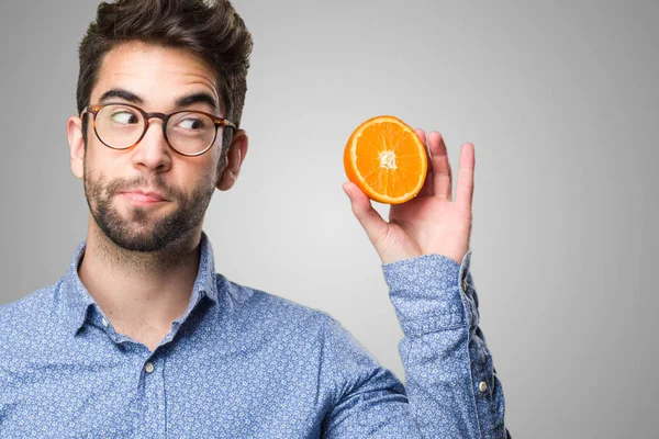 Mladý Muž Drží Pomeranč Šedém Pozadí — Stock fotografie