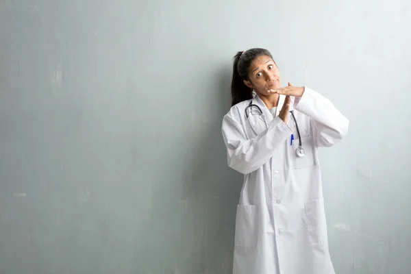 Young indian doctor woman against a wall tired and bored, making a timeout gesture, needs to stop because of work stress, time concept