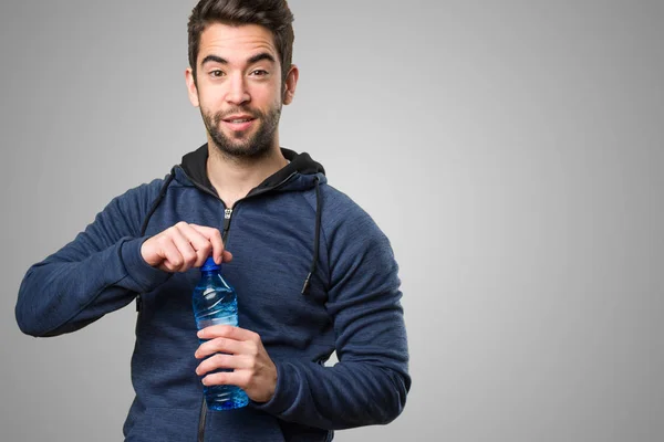 在灰色背景的快乐的年轻人拿着一瓶水 — 图库照片