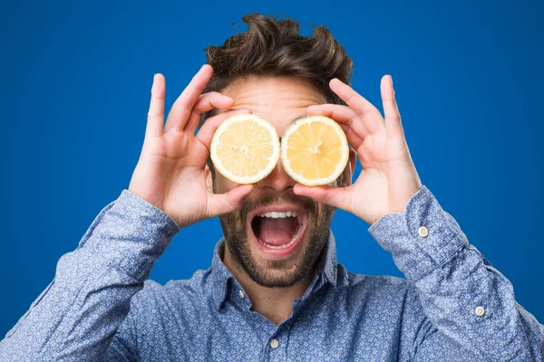 Junger Mann Bedeckt Seine Augen Mit Zitronen Auf Blauem Hintergrund — Stockfoto