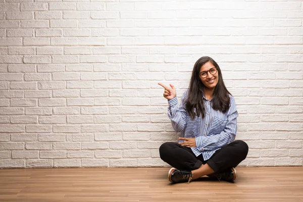 若いインド人女性座って笑って驚いて何か 自然に さりげなく提示側を指しているレンガの壁 — ストック写真