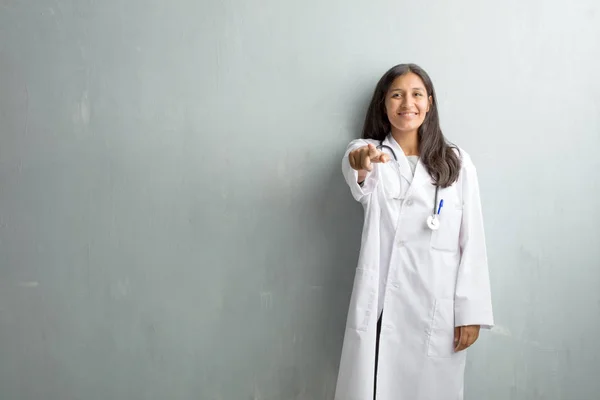Young indian doctor woman against a wall cheerful and smiling pointing to the front