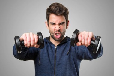 kızgın genç adam gri arka plan üzerinde dambıl kullanarak