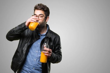 Genç adam gri arka plan üzerinde bir portakal suyu içme