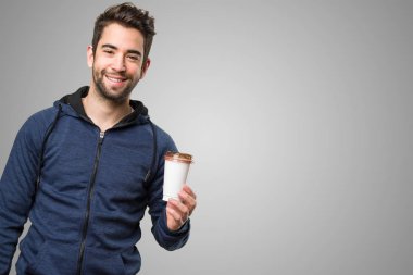 Genç adam bir kahve gri arka plan üzerinde tutan