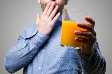 gri arka plan üzerine bir bardak meyve suyu tutan şaşırmış genç adam