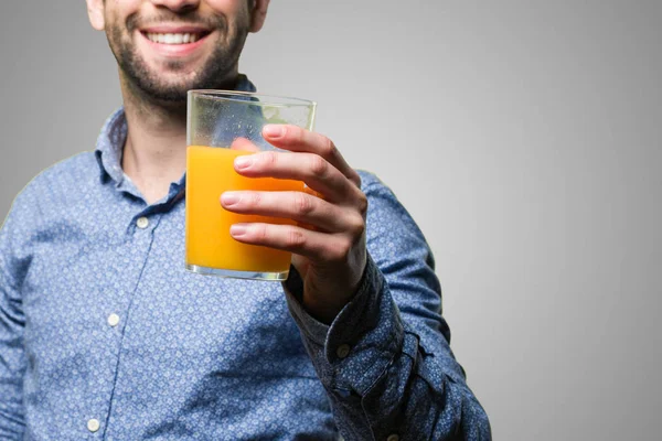 Genç adam gri arka plan üzerine bir bardak meyve suyu tutan