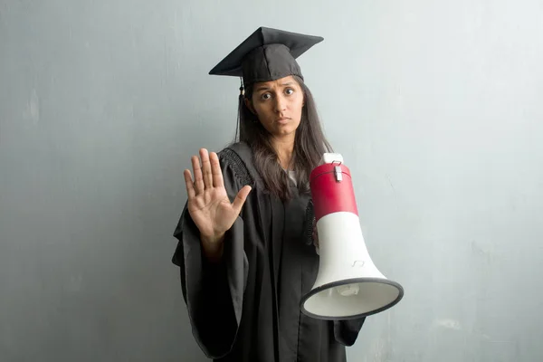Young graduated indian woman against a wall tired and bored, making a timeout gesture, needs to stop because of work stress, time concept. Holding a megaphone.