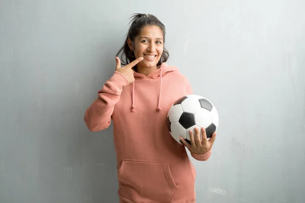 若いスポーティなインド女性壁笑顔に対して口 完璧な歯 白い歯の概念を指しては明るく陽気な態度 ゲームをプレイするサッカー ボールを保持しています — ストック写真
