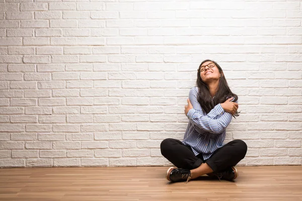 Young indian woman sit against a brick wall proud and confident, pointing fingers, example to follow, concept of satisfaction, arrogance and health